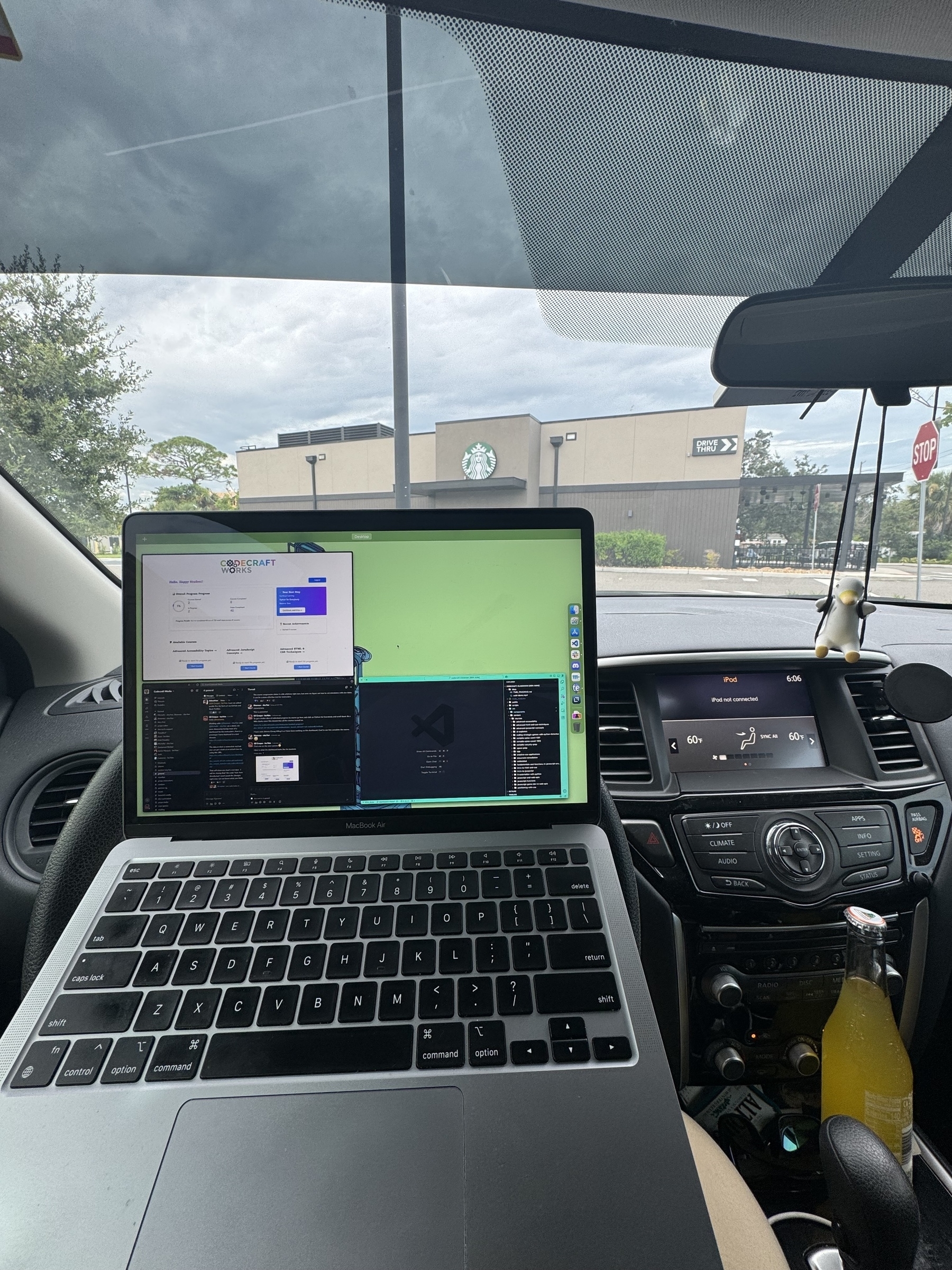 A person is using a laptop with coding software open, while parked in a car facing a Starbucks.