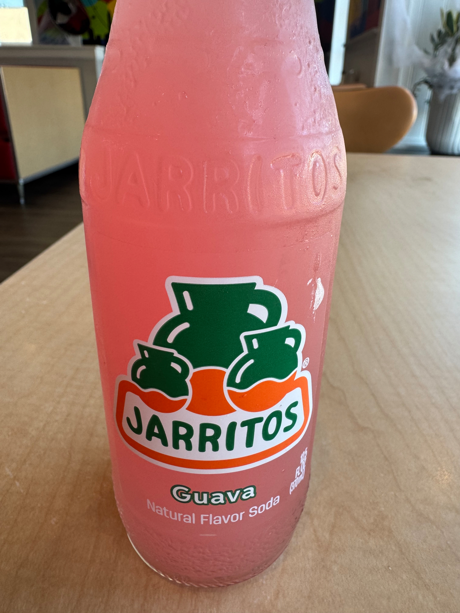 A bottle of Jarritos guava-flavored soda sits on a wooden table.