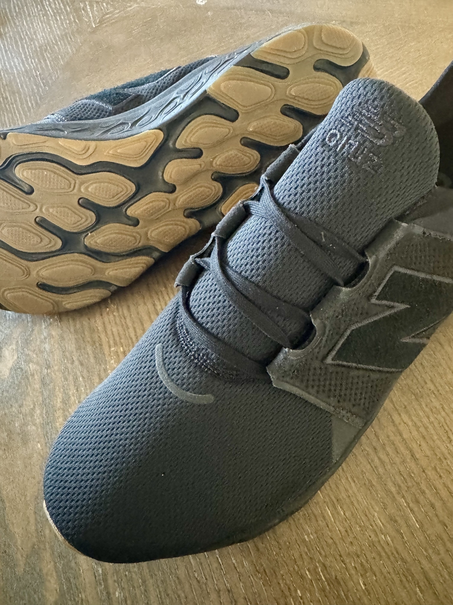 A pair of black athletic shoes with textured soles is placed on a wooden surface.