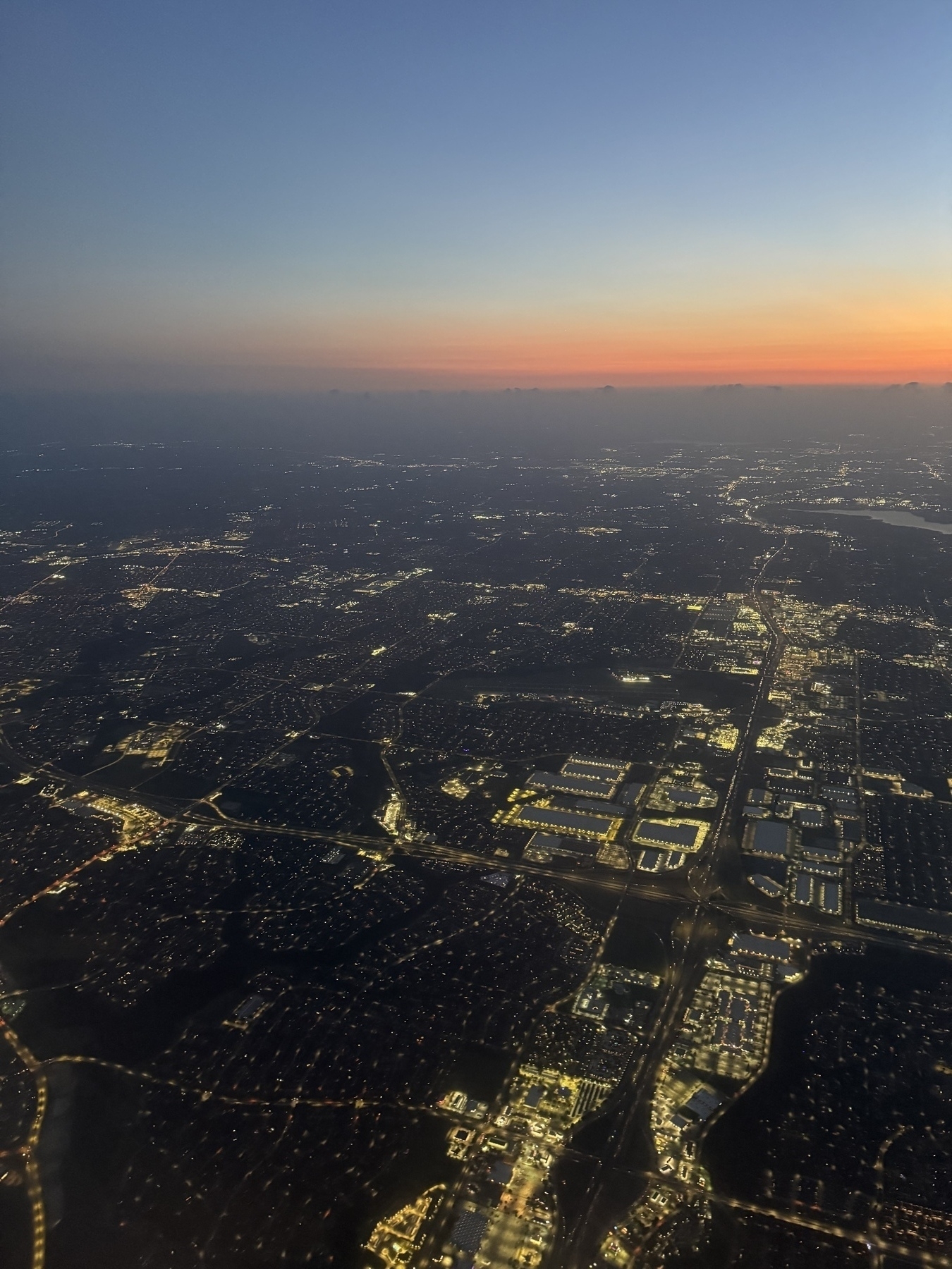 An aerial view captures a sprawling cityscape illuminated with lights under a twilight sky with a fading sunset.
